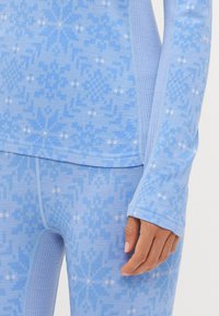 Ανοιχτό μπλε θερμική σετ με σχέδιο χιονονιφάδας, ριμπ υφή στους σφιγκτήρες και μαλακό ύφασμα. Ο σχεδιασμός περιλαμβάνει αντίθετους μπλε τόνους.