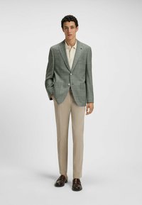 Grå rutiga kavaj med två knappar, i kombination med en krämfärgad polo-shirt och beige byxor. Bruna loafers kompletterar outfiten.