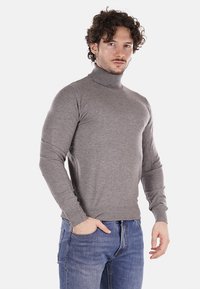 Maglione grigio a collo alto realizzato in tessuto lavorato a maglia, dalla vestibilità aderente, con maniche lunghe, polsini e orlo a costine, abbinato a jeans blu.