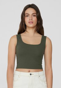 Top de tirantes de canale en verde oliva con escote cuadrado y ajuste corto, combinado con pantalones cortos de cintura alta de color claro. Sin patrones destacables.