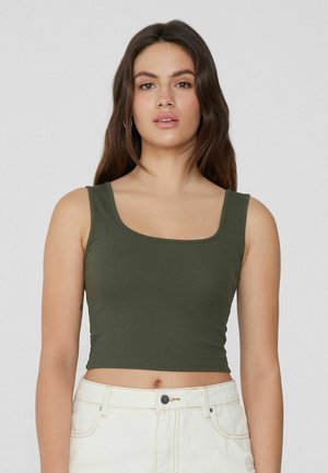 Olivengroene geribbelde tanktop met een vierkante halslijn en een cropped fit, gecombineerd met lichtgekleurde high-waisted shorts. Geen opvallende patronen.