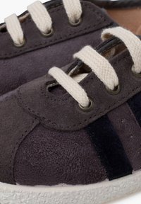 Sneaker in suede grigio scuro con lacci in cotone crema, con strisce blu navy e suola in gomma testurizzata. Sono presenti occhielli in metallo.