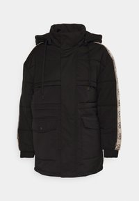 Giacca a vento nera con colletto alto, chiusura con zip, due tasche frontali e motivo decorativo beige lungo le maniche. Tessuto texture.