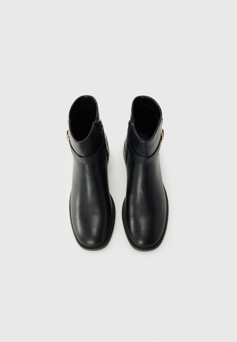 Botas de tobillo de cuero negro con un acabado suave, que cuentan con una cremallera lateral y una correa decorativa con un acento metálico. Diseño de suela plana.