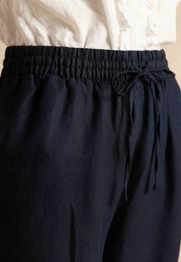 Tumesinised, kergekaalulised püksid, millel on elastne vöökoht ja nöörkinnitus. Sile tekstuur ja lai lõige, näidates peeneid kangavariatsioone.