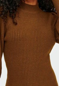 Pull marron côtelé avec un col montant et des manches longues, confectionné dans un matériau tricoté doux et texturé. Présente une silhouette ajustée.