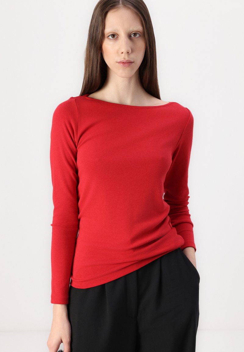 Haut rouge à manches longues en tissu doux, avec un col bateau et une coupe près du corps. Assorti à un pantalon noir ample.