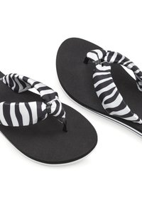 Schwarze Flip-Flops mit einer strukturierten Sohle, die gestreifte Stoffriemen aufweisen, die in der Mitte geknotet sind und abwechselnd schwarz und weiß sind.
