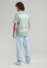 Minttuvihreä puuvillapaita, jossa on valkoinen kukkakuva ja teksti selkäpuolella. Vaaleansiniset löysät farkut ja valkoiset lenkkarit. Minimalistinen tyyli.