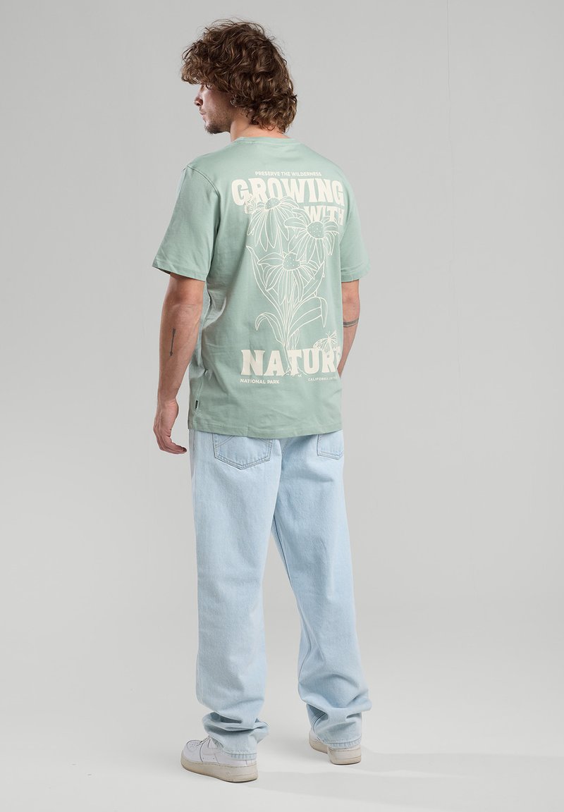 Minttuvihreä puuvillapaita, jossa on valkoinen kukkakuva ja teksti selkäpuolella. Vaaleansiniset löysät farkut ja valkoiset lenkkarit. Minimalistinen tyyli.