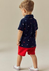 Marine polo t-shirt med farverige broderede mønstre, parret med røde shorts og hvide sneakers. Glat stof, korte ærmer, klassisk krave.