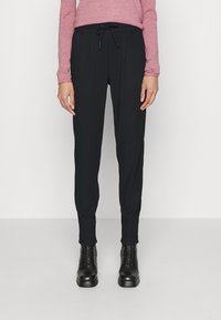 Calças pretas ajustadas com cintura elástica, apresentando pregas frontais e textura suave, combinadas com botas pretas de amarrar até ao tornozelo.