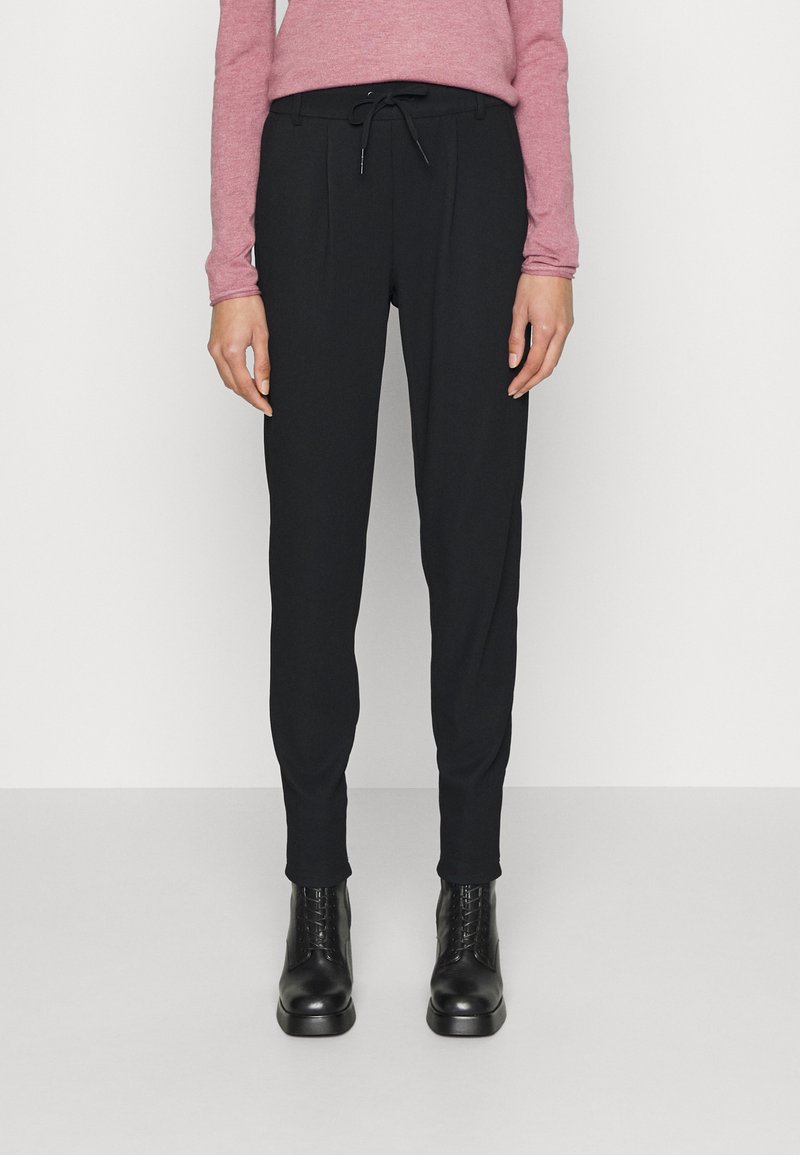 Calças pretas ajustadas com cintura elástica, apresentando pregas frontais e textura suave, combinadas com botas pretas de amarrar até ao tornozelo.