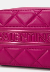 Prošívaná růžová kožená taška s lesklým, vyraženým logem "VALENTINO" na přední straně, s diamantovými vzory a precizním šitím.