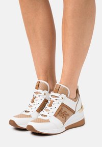 Scarpe sportive bianche e beige con un upper texturizzato, chiusura con lacci, dettagli dorati e suola ammortizzata. Presentano un logo sul lato.