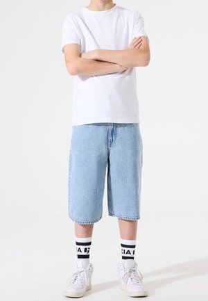 Weißes Baumwoll-T-Shirt, hellblaue Jeansshorts, weiße Sneaker und schwarz-weiß gestreifte Socken. Legeres Outfit mit lockerem Sitz.