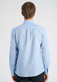 Lichtblauw longsleeve shirt met witte verticale strepen, met knoopmanchetten en een achterpand voor structuur. De stof lijkt textuur te hebben en is casual.