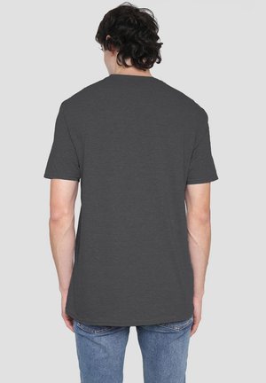 Man with dark curly hair wearing a plain dark gray short-sleeve t-shirt and blue jeans, facing away against a light gray background.