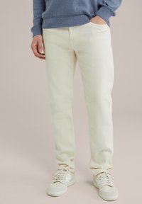 Pantalones de color claro con un corte relajado, hechos de algodón, que presentan una textura suave y bolsillos laterales, combinados con zapatillas deportivas blancas.