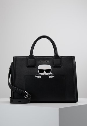 Schwarze Lederhandtasche mit Doppelgriffen, Fronttasche und einem Cartoon-Motiv einer Figur mit Sonnenbrille, die über die Tasche lugt.