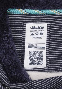 Label met een marineblauwe, fuzzy textuur en gestreepte stof. Bevat een veelkleurige rand, merknaam, QR-code en informatie over de maat.