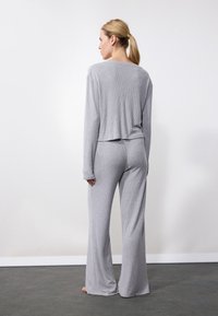 Set de loungewear gri, cu model cu nervuri, compus dintr-o bluză cu mânecă lungă și pantaloni largi. Textură moale, cu o croială relaxată și un design al bluzei scurte.