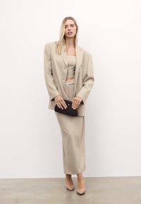 Bež blazer s krojem prevelikih dimenzij, v kombinaciji z usklajenim kratkim topom in krilom, dopolnjen z črnim clutchom in nude čevlji s pointed toe. Gladka tekstura.