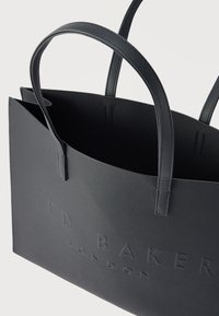 Μαύρη τσάντα tote με υφή και δύο λαβές, με ανάγλυφο λογότυπο "TED BAKER LONDON" στο μπροστινό μέρος και ανοιχτό σχεδιασμό στο πάνω μέρος.