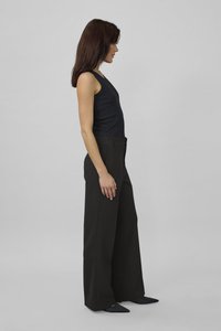 Top nero senza maniche abbinato a pantaloni neri a vita alta e gamba larga. Vestibilità slim in vita, tessuto morbido e scarpe nere a punta.