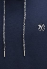 Dunkelblaues Sweatshirt mit strukturiertem Finish, ausgestattet mit Zugbändern im Fischgrätmuster und einem kleinen gestickten Logo auf der Brust.