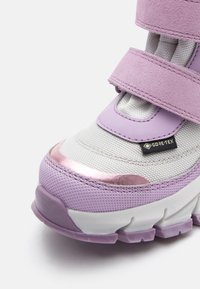 Fioletowe i białe sneakersy z rzepami, charakteryzujące się teksturowaną cholewką, błyszczącymi akcentami oraz etykietą Gore-Tex. Gruba gumowa podeszwa z dobrą przyczepnością.