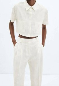 Chemise courte rayée blanche avec col et deux poches avant, associée à un pantalon large assorti. Le tissu semble doux et léger.