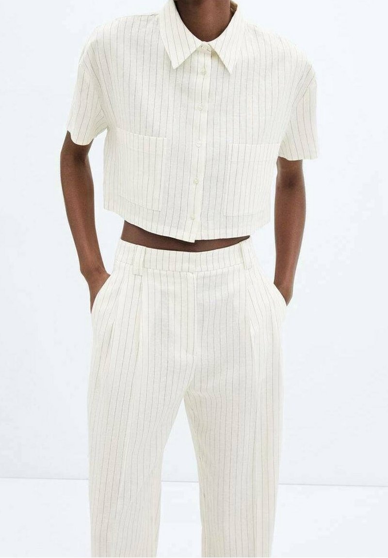 Chemise courte rayée blanche avec col et deux poches avant, associée à un pantalon large assorti. Le tissu semble doux et léger.
