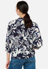 Marinebluse mit weißen Blumen- und Blattmustern, mit lockerer Passform, Dreiviertelärmeln und einem Rückenpasse-Detail. Strukturierter Stoff.