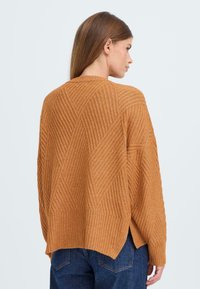 Pull en tricot orange rouillé avec une texture côtelée et un motif en diamant, présentant une coupe décontractée et des fentes sur le côté à l'ourlet.