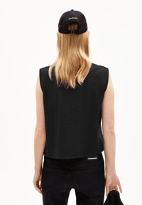 Black sleeveless top with a textured pattern, worn with dark jeans. The back features a tag with "ARMIDANSEL" and a cap with "CHANGE."
