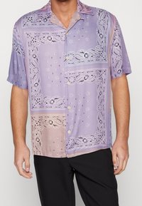 Krátký rukáv košile z lehké fialové tkaniny s paisley vzorem, knoflíky a kontrastní pastelové části.