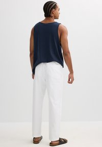 Top sin mangas de color azul marino con un corte holgado, combinado con pantalones rectos blancos y sandalias negras. Tejido suave y estilo casual.
