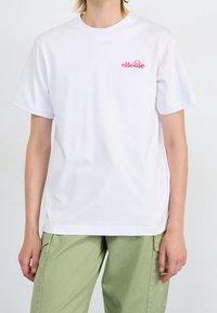 Witte katoenen t-shirt met een klein roze geborduurd "ellesse" logo op de borst. Standaard pasvorm met korte mouwen en een ronde halslijn.