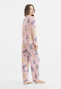 Conjunto de pijama rosa con estampados de animales y elementos celestiales en negro y amarillo. Tejido suave, manga larga y pantalones holgados.