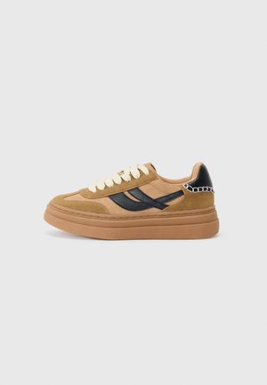 Brown suede sneakers with black accents, round toe, beige laces, and a thick gum sole. Features chain detail on the heel.