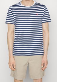 T-shirt rayé bleu marine et blanc avec un col rond et des manches courtes, arborant un petit logo rouge sur la poitrine.