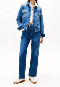 Modrá džínová bunda s knoflíkovým zapínáním, nošená přes krátké pruhované tričko. Modré džíny s vysokým pasem a střihem rovného střihu, doplněné bílými teniskami.