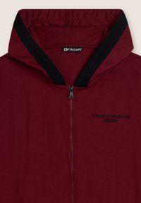 Sudadera con cremallera en burdeos de tejido suave, con un collar negro y la frase "HOY ES TU DÍA FREDDY" bordada en el pecho.