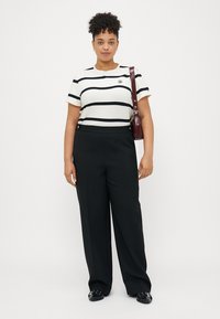 Mustavalkoraidallinen lyhythihainen paita, jossa on pyöreä pääntie, yhdistettynä korkeavyötäröisiin mustiin housuihin ja olkalaukkuun.