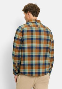 Karierter Hemd mit braunen, blauen, grünen und beigen Karos. Hergestellt aus gewebtem Stoff mit einem Button-down-Kragen und abgerundetem Saum.