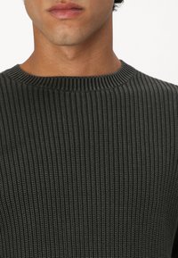 Tamsiai pilkas raukinis megztinis su apvalia iškirpte ir tekstūruotu audiniu, prigludęs prie kūno, su matomais siūlės detalėmis.