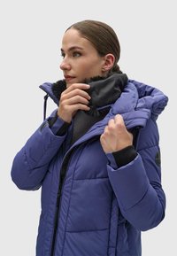 Violetti puhujal jacket mustalla turkiskollilla, jossa on vetoketjullinen etuosa ja hihansuut. Suunnittelussa on ommeltuja paneeleja ja logo- läppä.