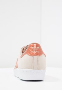 Beige sneakers met een gestructureerde koraalkleurige hieltab, witte rubberen zool en netstructuur. Heeft het Adidas-logo op de achterkant.