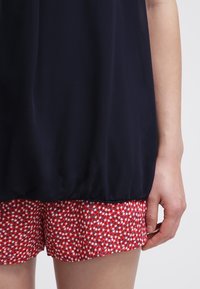 Haut léger bleu marine avec un ourlet froncé, associé à un short à imprimé floral rouge avec de petites touches blanches et bleues.